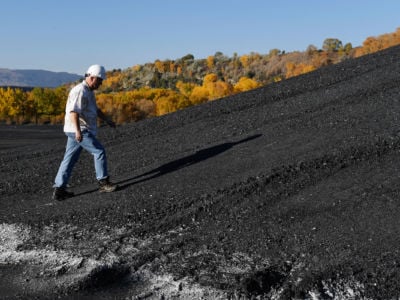 A man in a hard hat walks up a hill of coal