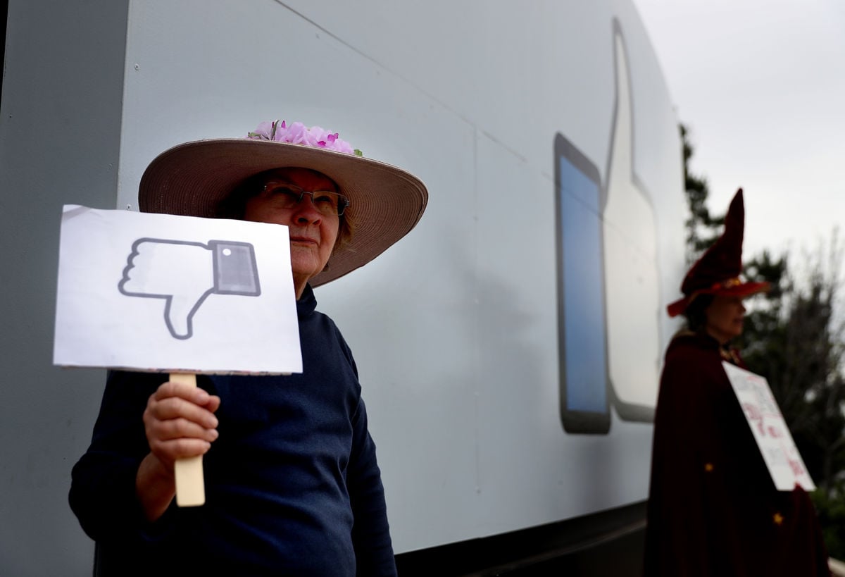 A protester stands outside of Facebook's headquarters holding a sign with a thumbs down icon