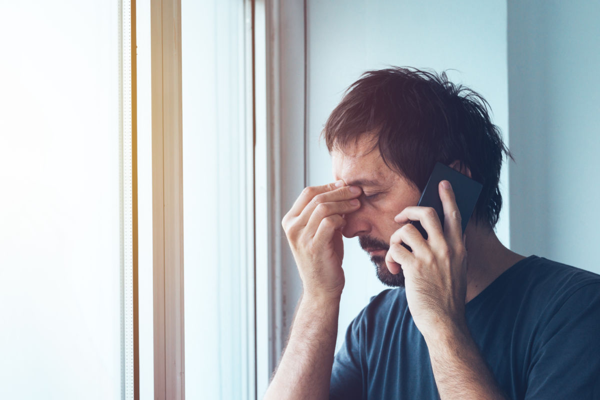 A man pinches the bridge of his nose during a cellphone call