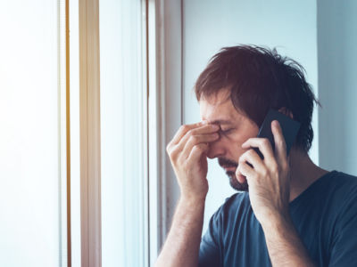 A man pinches the bridge of his nose during a cellphone call