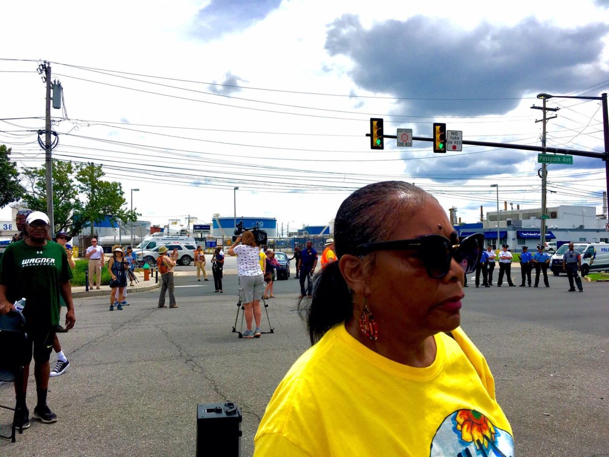 A woman in a yellow shirt is at the forefront of a protest in a wide street