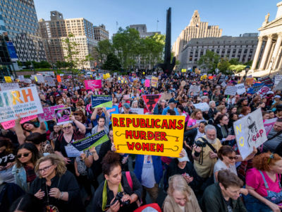 Someone in the middle of a protest holds a yellow sign reading "REPUBLICANS MURDER WOMEN"