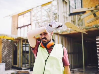 A construction worker wipes sweat from his forehead while squinting into the sun