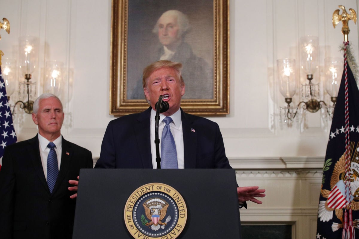 Donald Trump speaks into a microphone while Mike Pence stands beside him and a portrait of George Washington hangs behind him