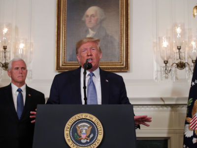 Donald Trump speaks into a microphone while Mike Pence stands beside him and a portrait of George Washington hangs behind him