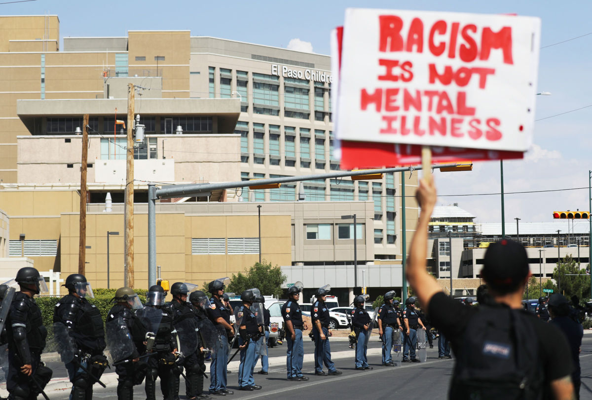 An anti-Trump protestor holds a sign as police are lined up outside University Medical Center, where President Trump was visiting shooting victims, following a mass shooting which left at least 22 people dead, on August 7, 2019, in El Paso, Texas.