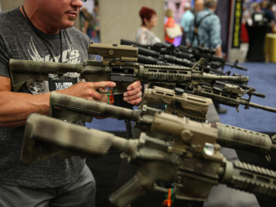 A man holds one of many guns on display at a gun expo