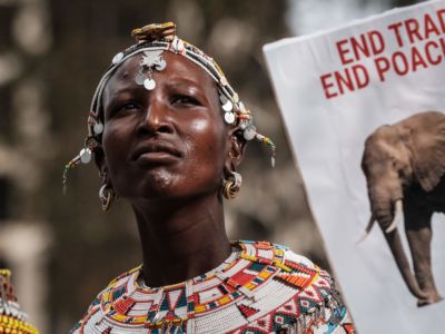 An Indigenous Kenyan woman stands near a sign denouncing elephant poaching during a protest