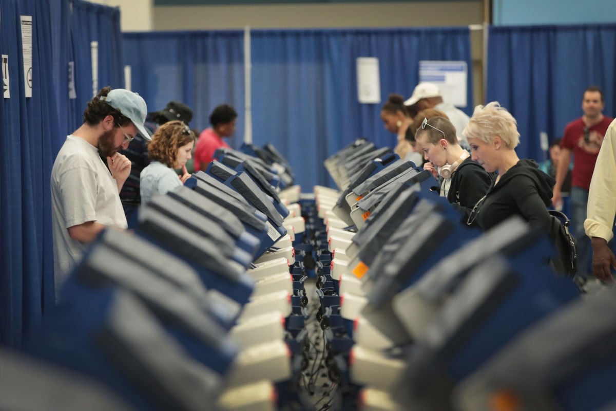 rows of people vote at blue electronic voting booths