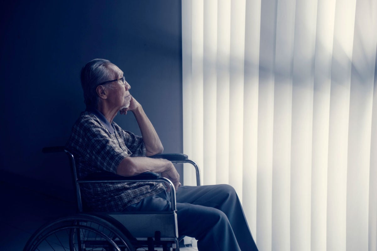An elderly man sits next to a window while sitting in a wheelchair
