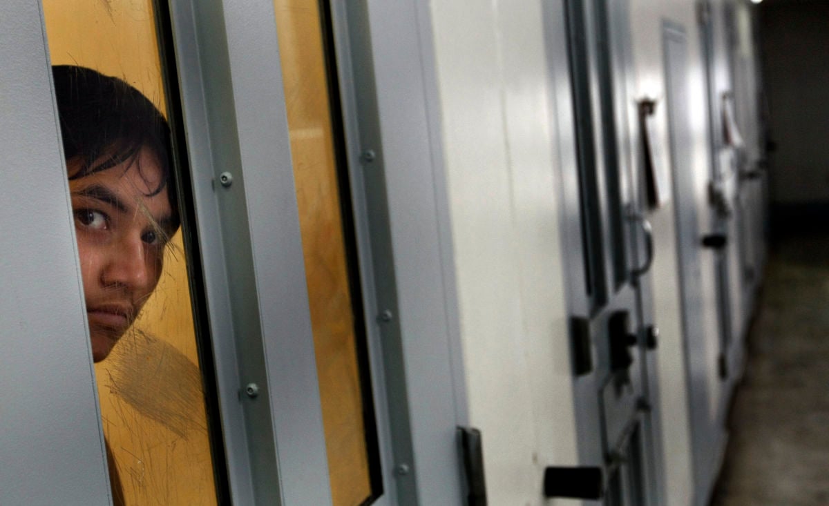 A prisoner peers through a narrow window in their solitary confinement cell