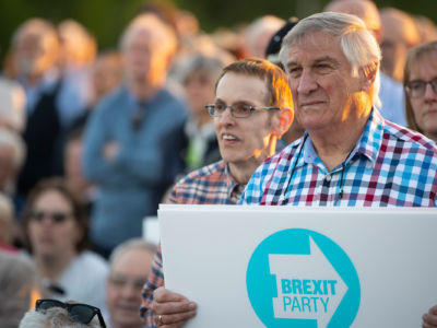 An elderly white man holds a pro-brexit sign during a rally while listening sternly