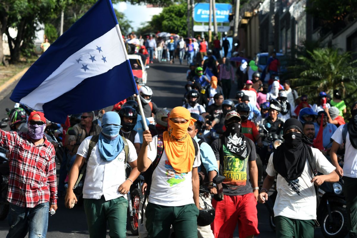Masked protesters march in the streets while wavind a Honduran flag