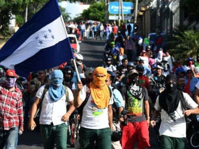 Masked protesters march in the streets while wavind a Honduran flag