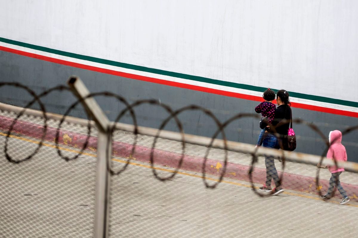 A mother walks with two children near a wall with barbed wire fence
