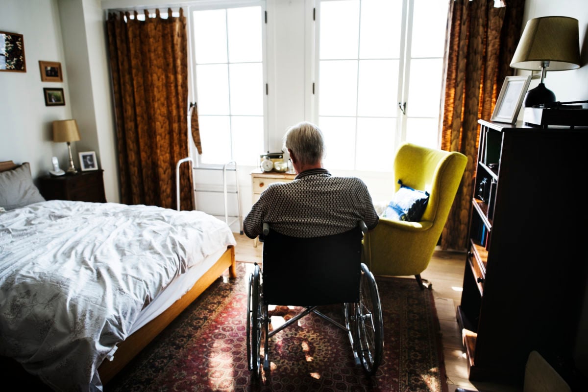 An elderly man sits in a wheelchair in a bedroom