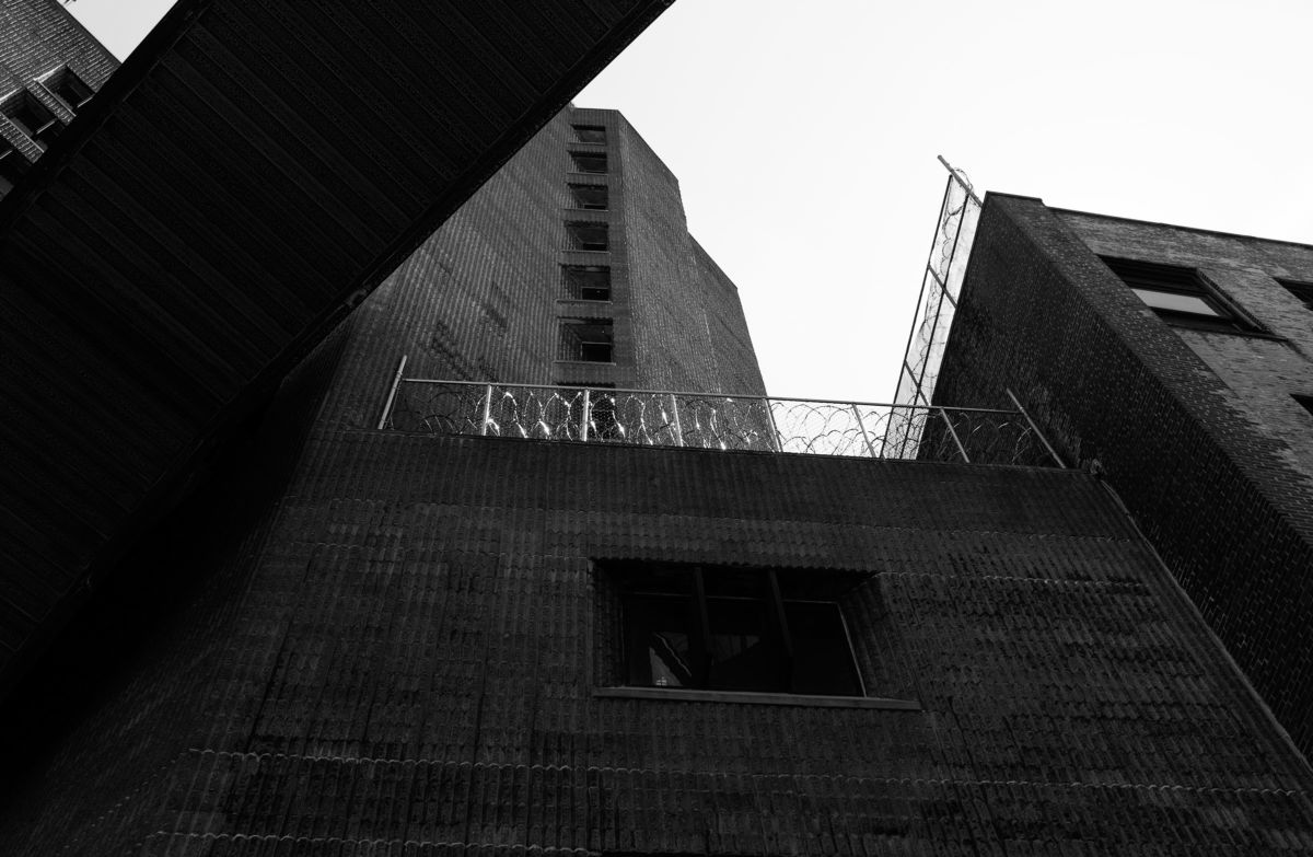 An exterior shot of the Manhattan Correctional Center, a brick building festooned with barbed wire