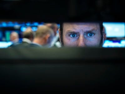 Stock broker's eyes are seen through the gap of the computer screens he's working at