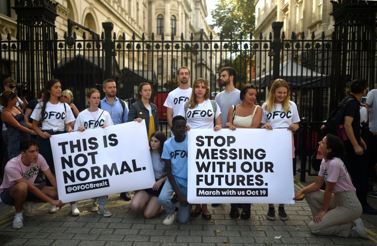 People hold signs reading "THIS IS NOT NORMAL" and "STOP MESSING WITH OUR FUTURES" during a protest