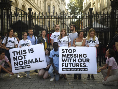 People hold signs reading "THIS IS NOT NORMAL" and "STOP MESSING WITH OUR FUTURES" during a protest