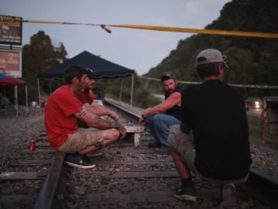 Men sit on railroad tracks cordoned off with police tape