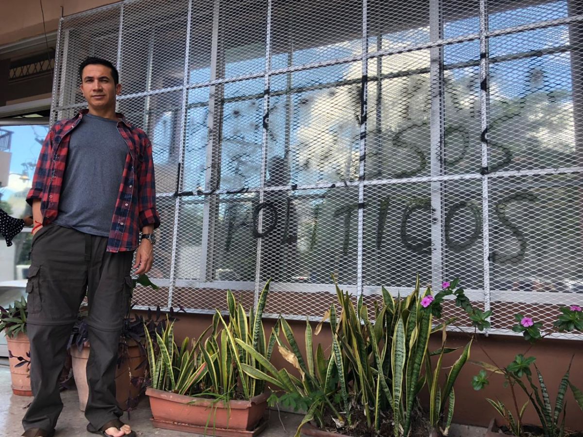 Edwin Espinal stands before the Honduran attorney general's office, which has been marked with graffiti that reads, "Freedom for political prisoners,"