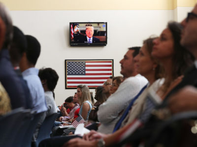 President Donald Trump is seen on a television screen as he makes a taped speech during a ceremony for people to become American citizens at a U.S. Citizenship and Immigration Services naturalization ceremony in a Miami Field Office on August 16, 2019, in Miami, Florida.