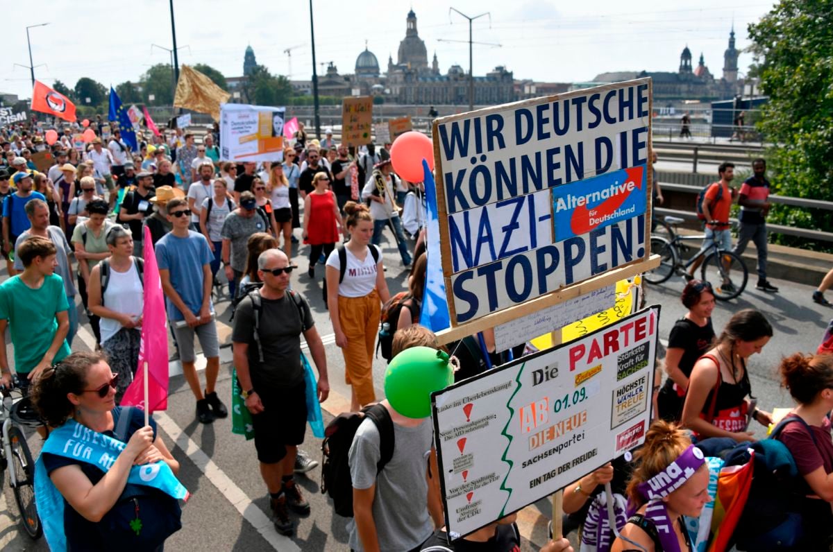 A crowd of protesters walk together in a street displaying signs in German