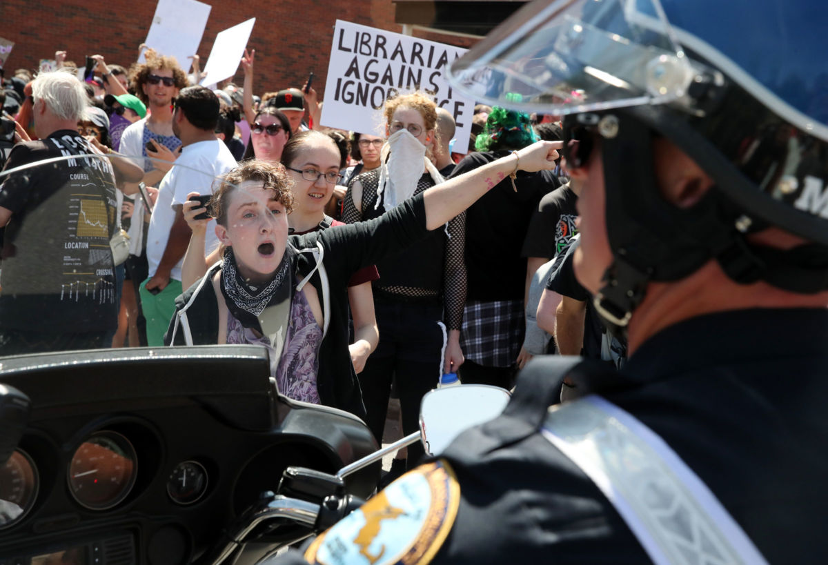 A protester yells while pointing out of frame to a police officer in the foreground