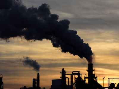 Smoke pours from smokestacks silhouetted against the sunset