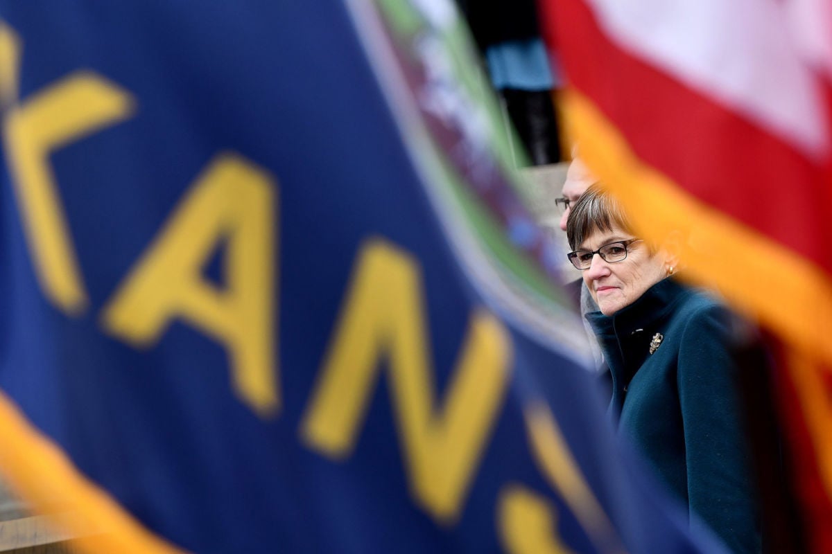 Laura Kelly is seen through a space between the kansas and U.S. flags