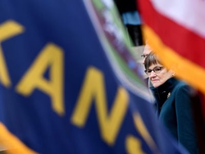 Laura Kelly is seen through a space between the kansas and U.S. flags
