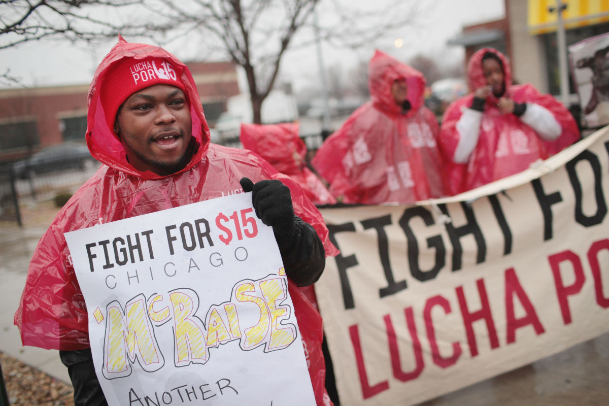 Several protesters display signs outside of a McDonalds while wearing red rain ponchos