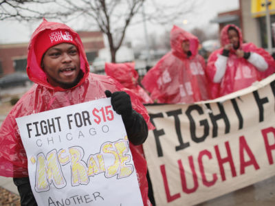 Several protesters display signs outside of a McDonalds while wearing red rain ponchos