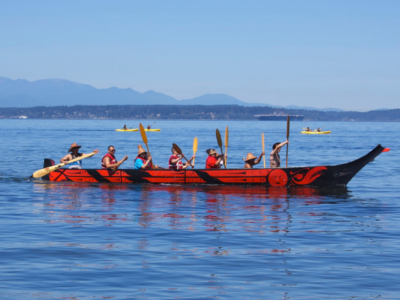 seven people row in a canoe painted with red and black designs