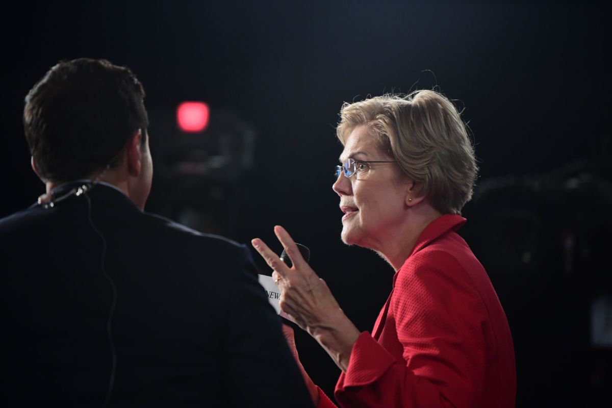 Elizabeth Warren speaks to members of the press in a darkened room, debate