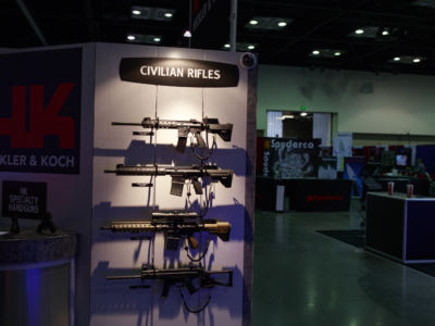 A spotlight shines on a wall displaying Heckler & Koch "civilian rifles" at a gun show