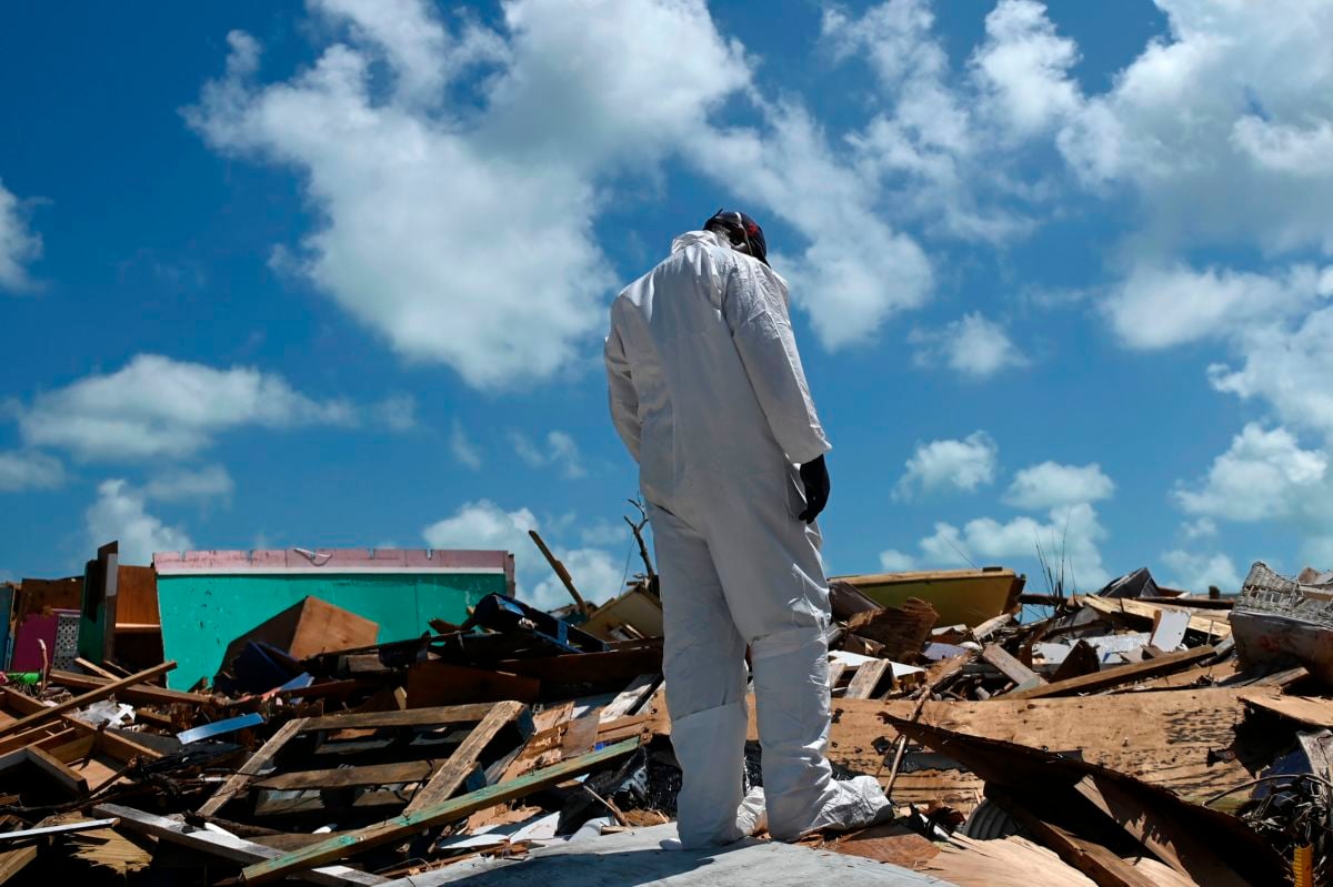 A man in a white HAZMAT suit stands on top of rubble