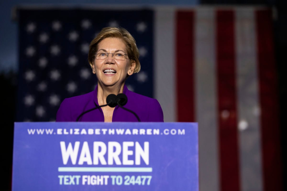 Sen. Elizabeth Warren speaks to a crowd while standing in front of a U.S. flag