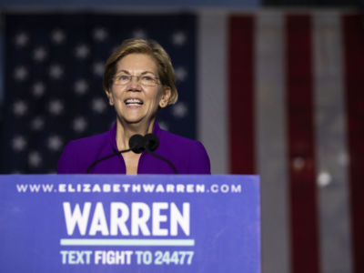 Sen. Elizabeth Warren speaks to a crowd while standing in front of a U.S. flag