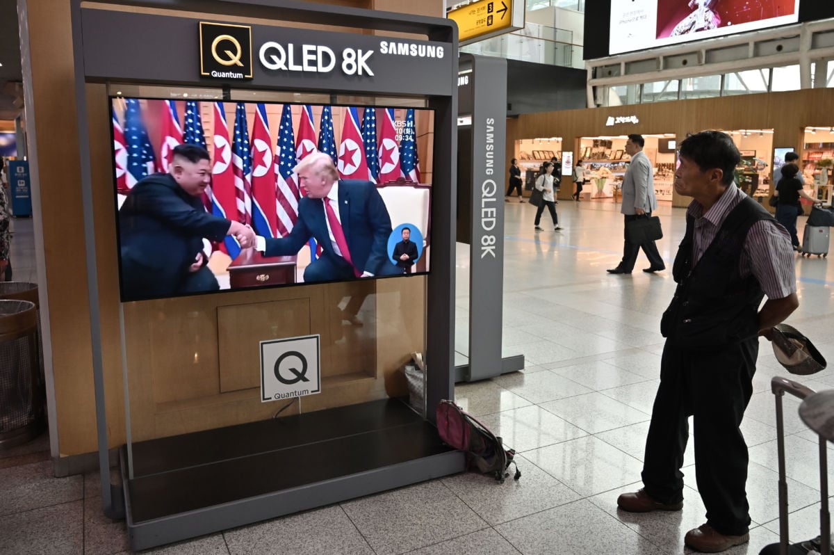 A man watches a tv screen showing Kim Jong Un speaking with Donald Trump