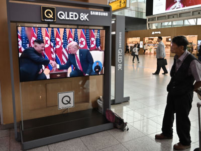 A man watches a tv screen showing Kim Jong Un speaking with Donald Trump