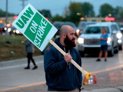 A man holds a sign reading "UAW ON STRIKE"