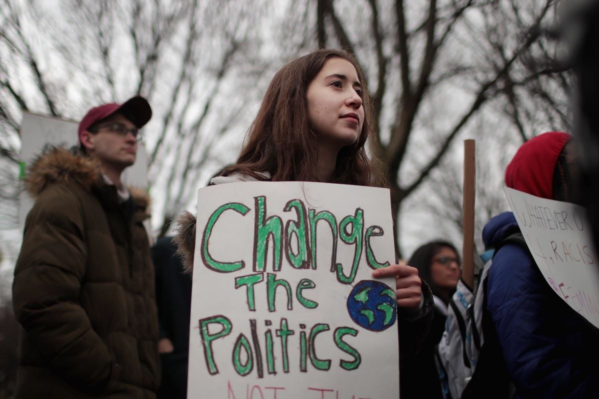 An activist displays a sign reading "CHANGE THE POLITICS" with a drawing of the planet Earth
