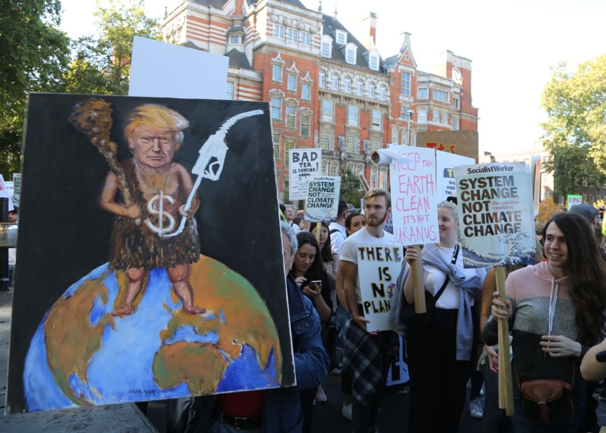 An activist displays a painting of trump wearing a loincloth holding a gas pump in one hand and a club in the other