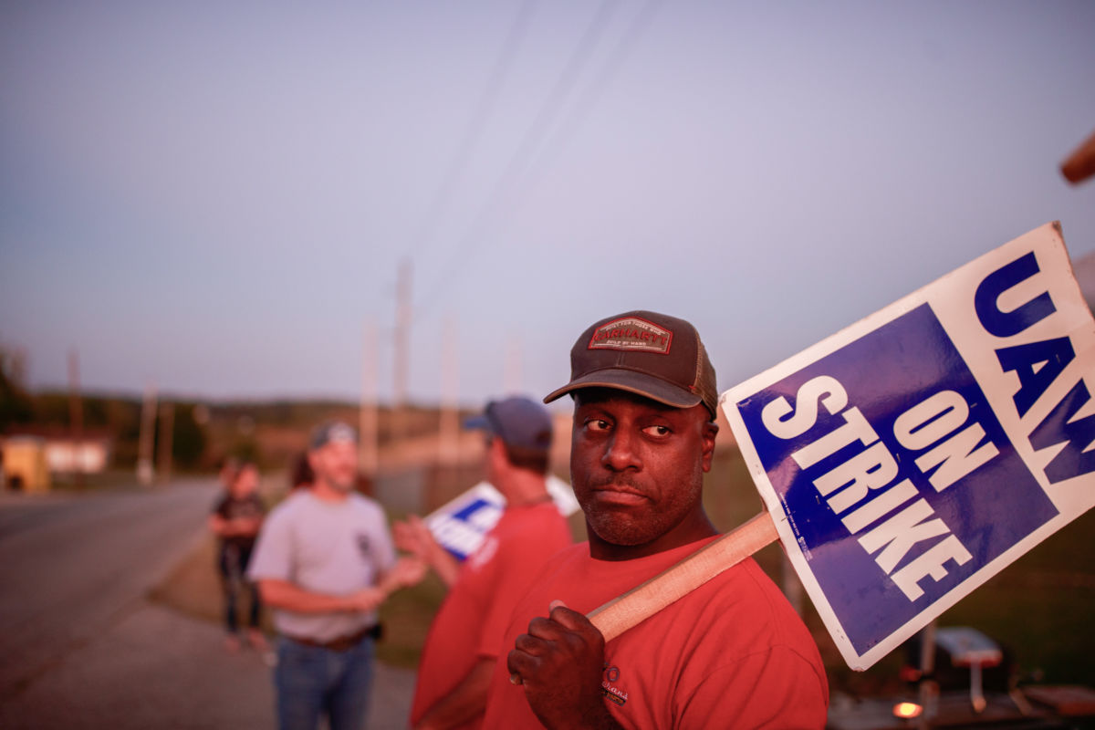 Workers from United Auto Workers Local 440 picket outside the General Motors Bedford Powertrain factory, where parts are molded from liquid metal, as the sun sets on day three of a nationwide worker strike against General Motors (GM).
