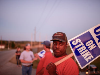 Workers from United Auto Workers Local 440 picket outside the General Motors Bedford Powertrain factory, where parts are molded from liquid metal, as the sun sets on day three of a nationwide worker strike against General Motors (GM).