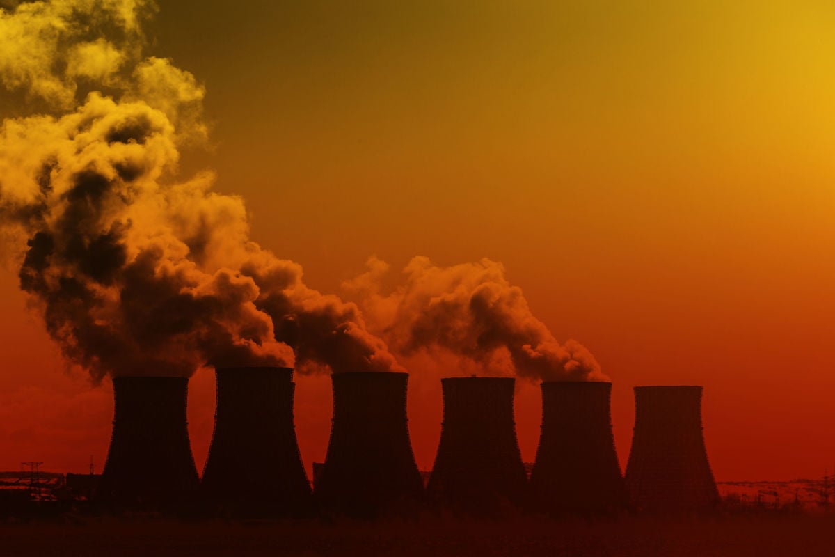 Nuclear cooling towers blow steam into the air against a red sky