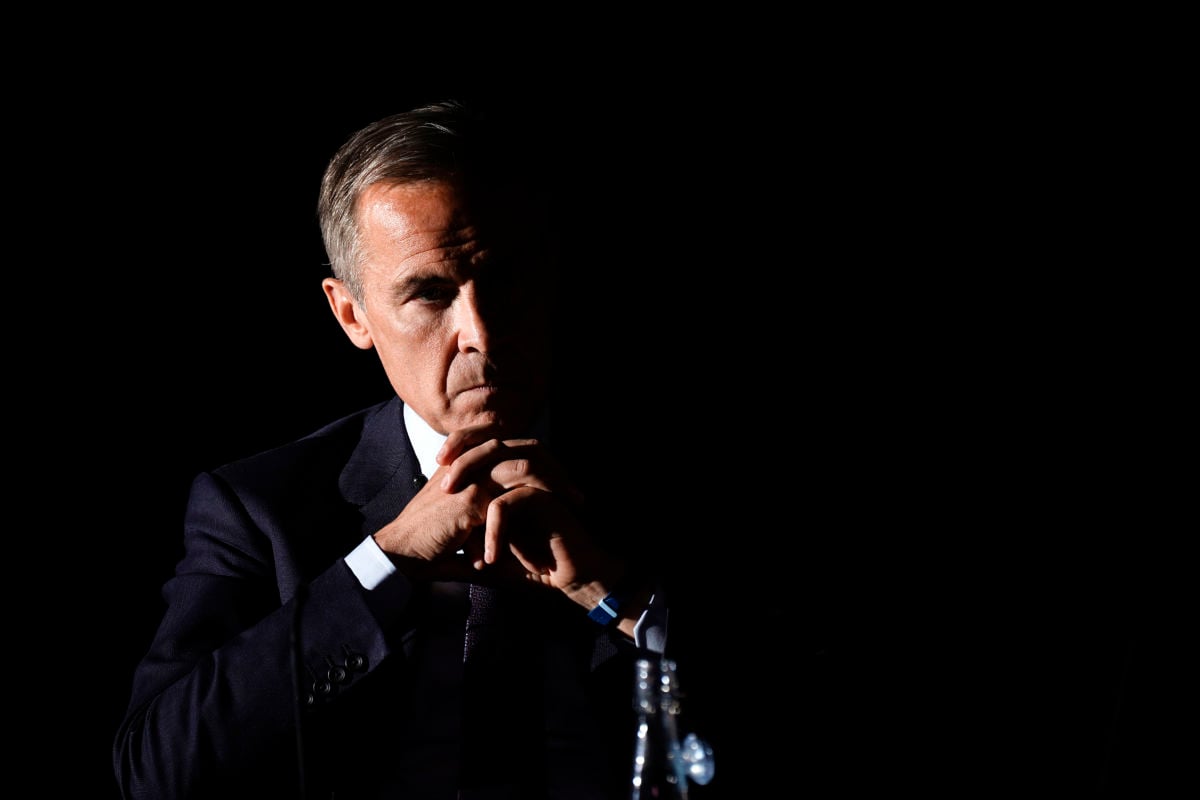 Mark Carney's face is partially obscured by shadow as he sits in a chair