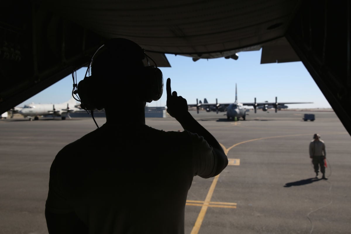 A soldier is silhouetted against the sky from within the loading dock of an airplane